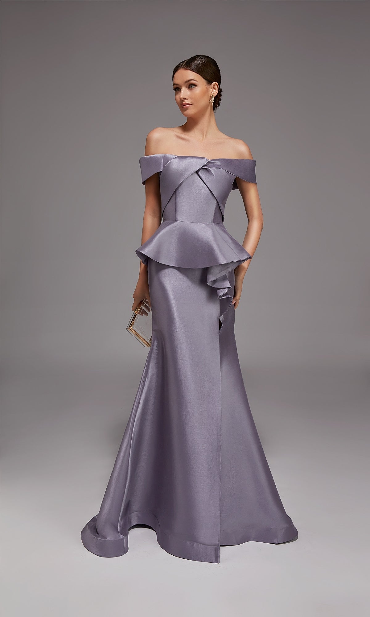 A woman in the Alyce 27827 long formal dress, lilac grey, with an off-the-shoulder peplum design, holds a small clutch while standing against a plain gray background.